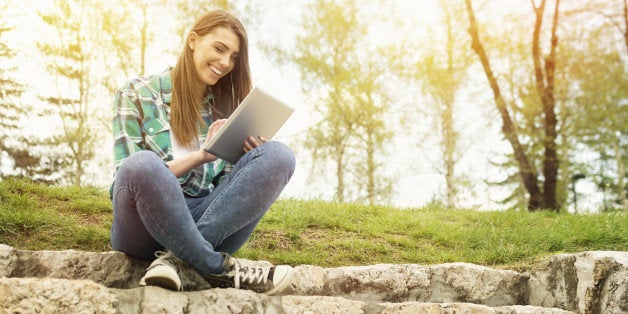 Beautiful young Caucasian brunette woman with tablet sitting on stairs in park wearing modern casual clothes and canvas shoes.