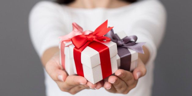 Woman holding a small gift box in a gesture of giving. Christmas holiday or special occasion gift box with red, purple and pink ribbon.