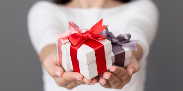 Woman holding a small gift box in a gesture of giving. Christmas holiday or special occasion gift box with red, purple and pi