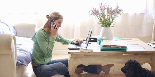 Mid adult woman sitting on floor, leaning on sofa, talking on, using laptop, side view