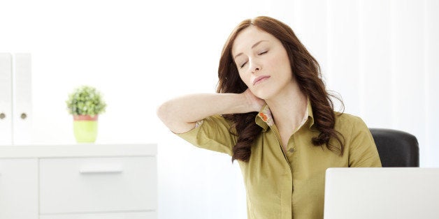 Young Businesswoman Having Neckache in the office, doing massage of the neck and sitting at the desk.