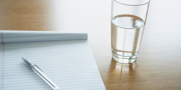 Notepad with a pen lying on it and glass of water on a table