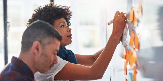 A businessman and businesswoman brainstorming on a whiteboard in a tech start-up office