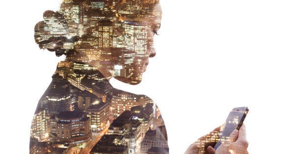 Double exposure of a business woman using a smart phone, and a view of the financial district of the City of London at night.