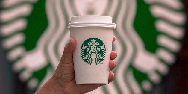 CHENGDU, SICHUAN PROVINCE, CHINA - 2015/09/13: Hand holding a cup of coffee in front of Starbucks logo. Starbucks is streamlining the ordering process so customers are able to get that cup of coffee faster than usual. (Photo by Zhang Peng/LightRocket via Getty Images)