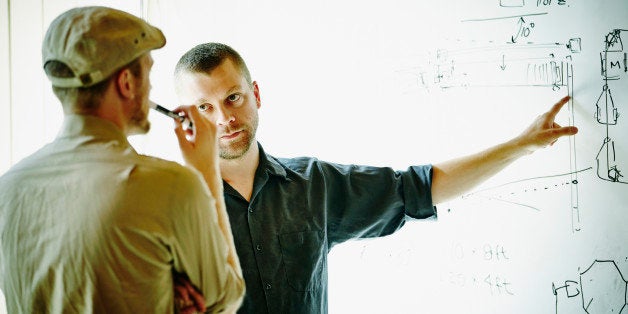 Two engineers discussing project design on whiteboard in startup office