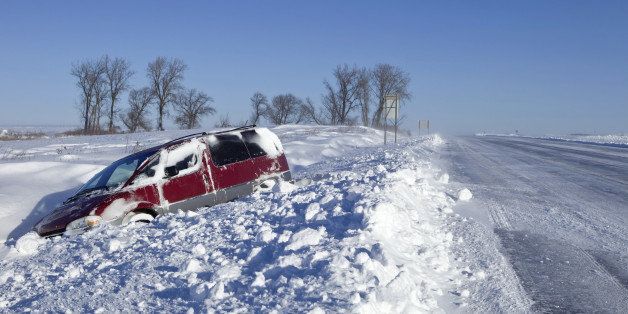 A minivan is stuck in the ditch of a deserted four lane highway. This image was taken shortly after a snowstorm with severe blizzard conditions. Snow continues to blow and is visible in the background