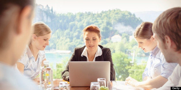 Group of young business people together in a business meeting, working on their new project on the computer laptop. Beautiful natural panorama through the big glass panorama window of the conference room. Selective Focus on young woman typing on computer notebook.