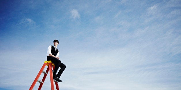 Businessman sitting on top of ladder wearing sunglasses looking out