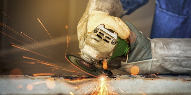 Electric wheel grinding on steel structure by worker in factory.