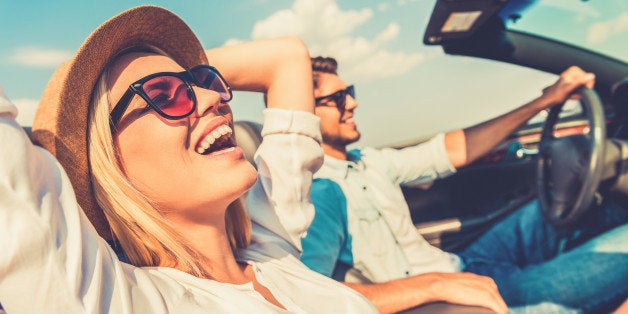 Side view of joyful young woman relaxing on the front seat while her boyfriend sitting near and driving their convertible