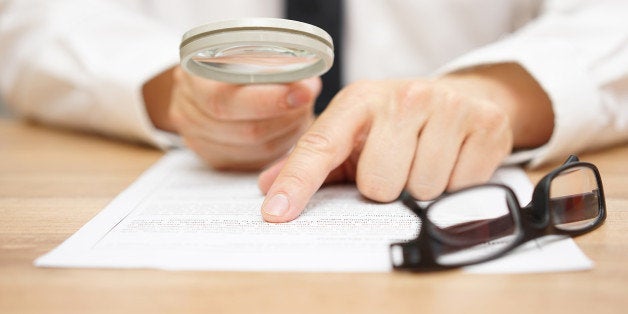 Focused businessman is reading through magnifying glass document