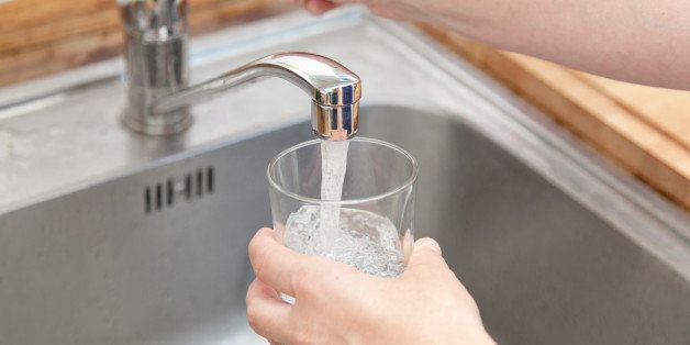 woman holding glass at water tap and filling water.