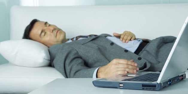 Businessman sleeping on sofa, hand resting on laptop