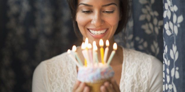 Hispanic woman looking down at lit candles on birthday cupcake