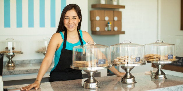 Cute young Hispanic woman standing across the counter in her cake shop and smiling