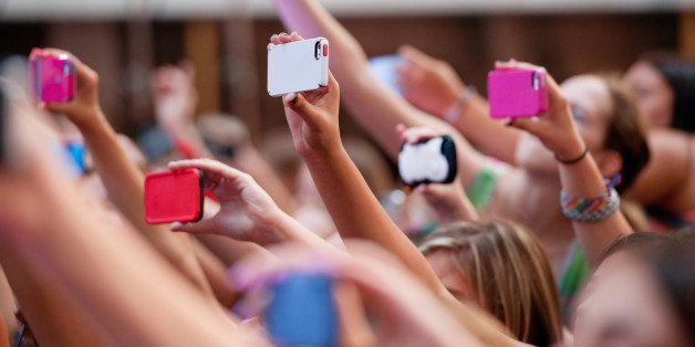 Side view of a group of people in a crowd using different brands and colors of mobile phones (cellphones).