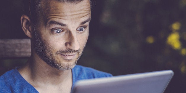 Man using tablet pc in the garden, looking surprised.