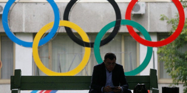 A man uses his tablet computer as he sits near Olympic rings placed in the courtyard of the Russian Olympic Committee headqua