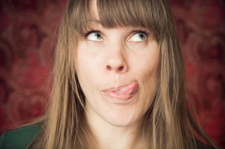 A woman makes a silly face by sticking her tongue out and looking up.