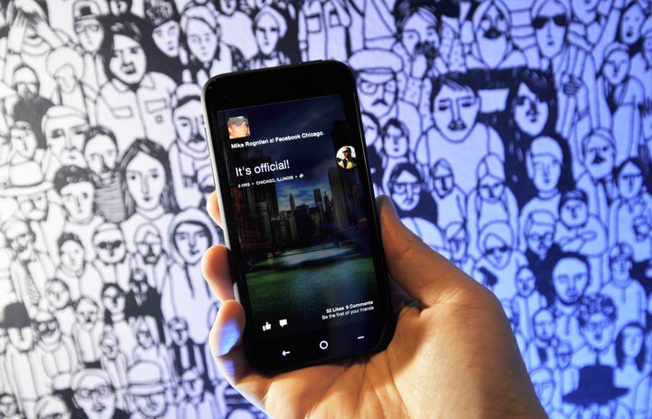 A Facebook employee displays an HTC phone with the new Home operating system against the backdrop of a decorated wall at Facebook's Headquarters office in Menlo Park, California on April 04, 2013. Facebook on Thursday unveiled a software suite which stakes out a 'home' on Android smartphones as it steps up its challenge to Apple and Google in the booming mobile market. Facebook called the new software 'a new way to turn your Android phone into a great, living, social phone.' The software, which allows users to see Facebook's 'Cover Feed' when they turn on their phones, will be available for download from Google's online Play shop in the United States starting April 12, Zuckerberg said. AFP PHOTO / Josh EDELSON (Photo credit should read Josh Edelson/AFP/Getty Images)