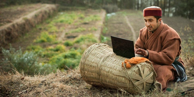 People of Himachal Pradesh: Young farmer using laptop, he is sitting in terraced field wearing traditional winter dress of Himachal Pradesh and the laptop placed on a basket made of bamboo.