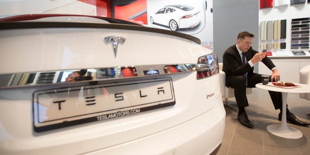 Elon Musk, billionaire, co-founder and chief executive officer of Tesla Motors Inc., checks a mobile device as a Tesla Model