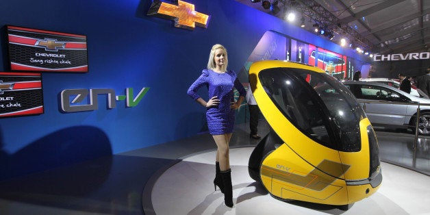 NEW DELHI, INDIA - JANUARY 5: A model poses with a Chevrolet Concept Car EN-V (Electric Networked Vehicle) during the 11th Auto Expo 2012 at Pragati Maidan on January 5, 2012 in New Delhi, India. This two-seat car is powered by two electric motors (one for each wheel) and can drive, maneuver around obstacles and park itself using advanced technology navigation system like GPS, sensors & continuous communication with other EN-Vs. The car is about 1.5 meters long and weigh less than 500 kilograms. (Photo by Virendra Singh Gosain/Hindustan Times via Getty Images)