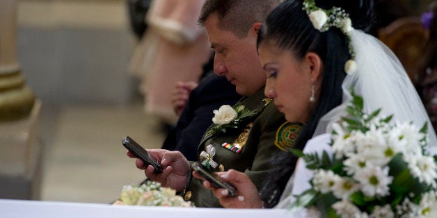 A bride and groom use their mobile phones during a mass wedding of police officers at the Cathedral of Bogota, on December 9, 2011. Ninety-six couples are getting married in the same ceremony. AFP PHOTO/Luis ACOSTA (Photo credit should read LUIS ACOSTA/AFP/Getty Images)