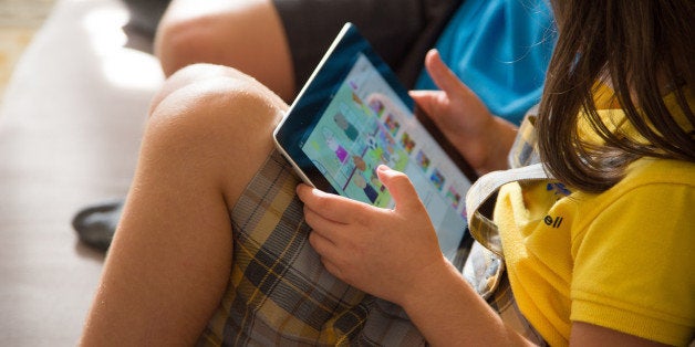 Boy and girl watching cartoons online with the iPad tablet sitting in the sofa at home.