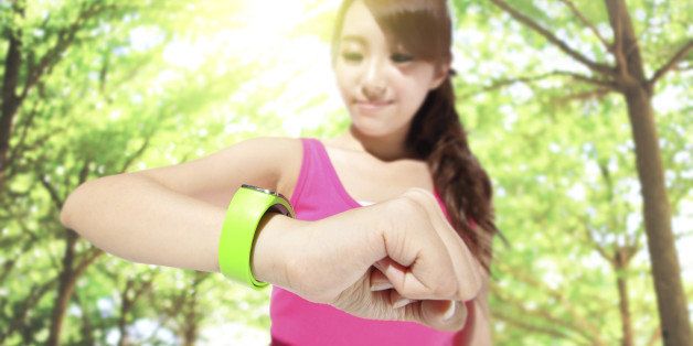 Health sport woman wearing smart watch device with touchscreen doing exercises with green tree background, focus on watch, asian