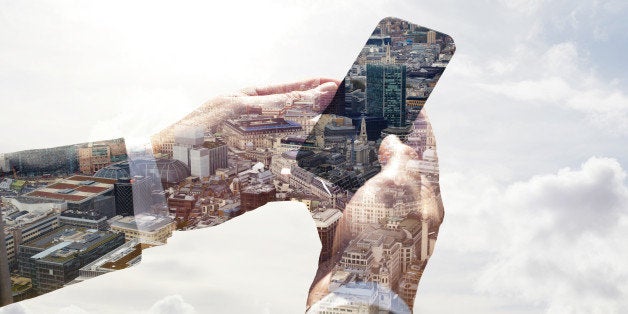 Double exposure of a business man using a smart phone with a view of the city of London and the sky.