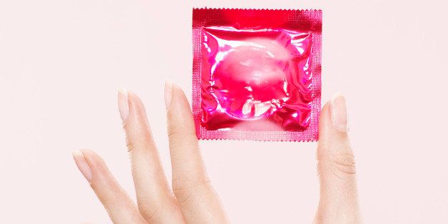 female hand, pink condom packet, condom, pink background