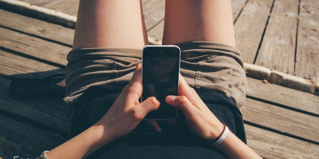 A girl texting on an iPhone on a dock.