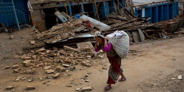 A Nepalese woman carrying belongings walks past a damaged house in Chautara, Nepal, Wednesday, May 13, 2015. The condition of many of the buildings damaged in the April 25 earthquake, got worse after the magnitude-7.3 quake Tuesday. (AP Photo/Bernat Amangue)