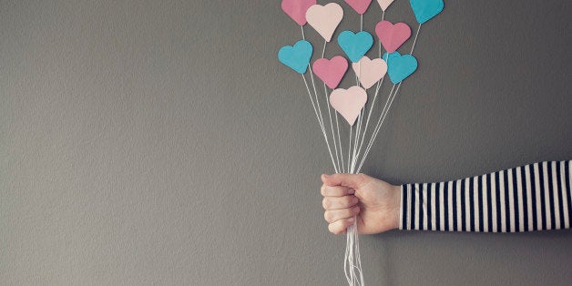 A hand holding the strings of a bunch of blue & pink paper hearts like they are balloons.