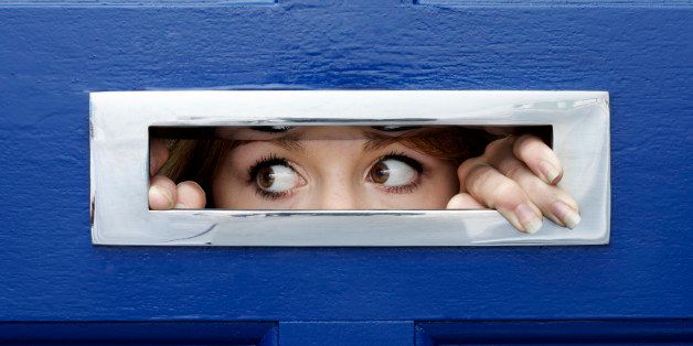 Young woman oeering out of letterbox in front door of house