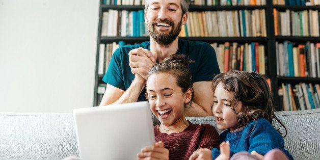 laughing little family on sofa looking tv at tablet computer