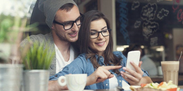 Embracing couple using mobile phone in cafe