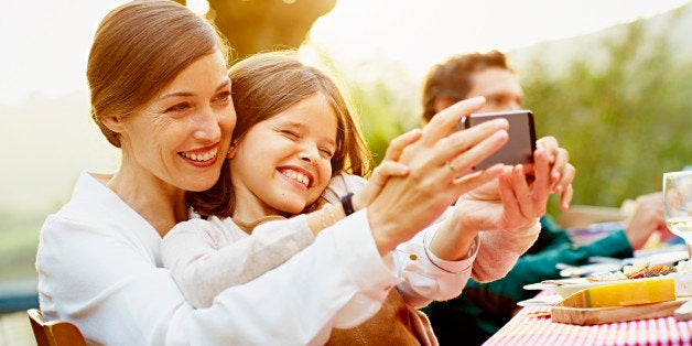 Happy mother and daughter taking selfie through smart phone at outdoor table in yard