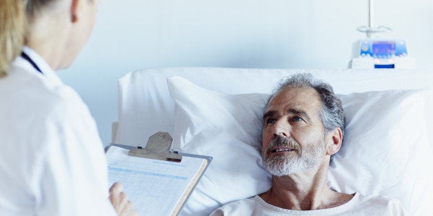 Female doctor writing notes while talking to male patient in hospital ward