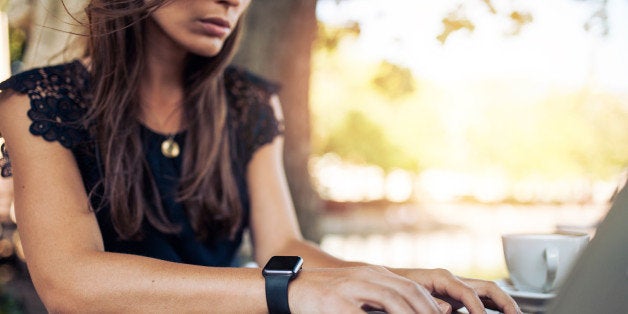 Young woman wearing smartwatch using laptop computer. Female working on laptop in an outdoor cafe.