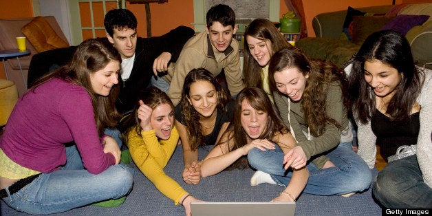 Friends looking at laptop on rug in living room, laughing