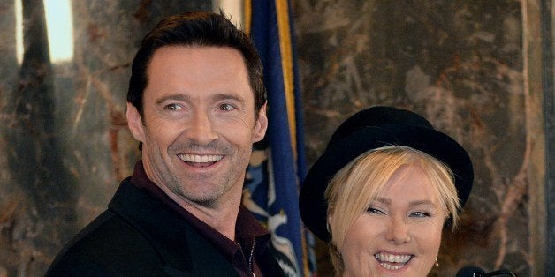 Hugh Jackman (C) and wife Deborra-lee Furness (R) before fliping a switch to ceremoniously light the Empire State Building lights January 24, 2014 in the lobby of the building in New York. The bulding will be lit in green and gold in honor of Australia Day, January 26. AFP PHOTO/Stan HONDA (Photo credit should read STAN HONDA/AFP/Getty Images)