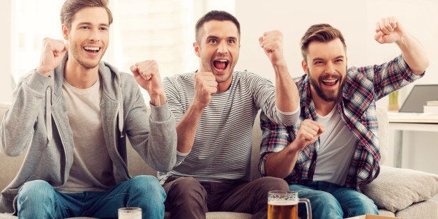 Three happy young men watching football game and keeping arms raised while sitting on sofa