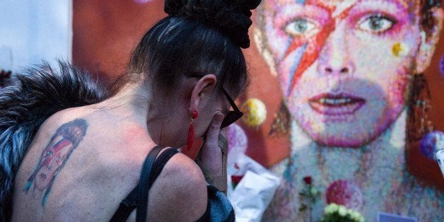 A woman with a tatoo of David Bowie reacts as she pays her respects in front of the British singer, painted by Australian street artist James Cochran, aka Jimmy C, following the announcement of Bowie's death, in Brixton, south London, on January 11, 2016. British music icon David Bowie died of cancer at the age of 69, drawing an outpouring of tributes for the innovative star famed for groundbreaking hits like 'Ziggy Stardust' and his theatrical shape-shifting style. AFP PHOTO / JUSTIN TALLISRESTRICTED TO EDITORIAL USE, MANDATORY MENTION OF THE ARTIST UPON PUBLICATION, TO ILLUSTRATE THE EVENT AS SPECIFIED IN THE CAPTION / AFP / JUSTIN TALLIS (Photo credit should read JUSTIN TALLIS/AFP/Getty Images)