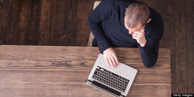 A direct over head view of a man working on a laptop at a wooden table.