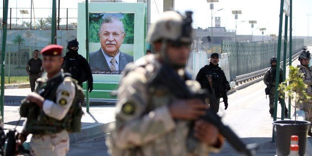 Iraqi soldiers stand guard next to a portrait of the Iraqi President at a checkpoint outside the presidential compound as the