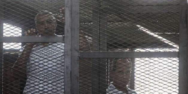 Australian journalist Peter Greste (R) of Al-Jazeera his colleagues stand inside the defendants cage during their trial for allegedly supporting the Muslim Brotherhood at Cairo's Tora prison on March 22, 2014. The high-profile case that sparked a global outcry over muzzling of the press is seen as a test of the military-installed government's tolerance of independent media, with activists fearing a return to autocracy three years after the Arab Spring uprising that toppled Hosni Mubarak. AFP PHOTO / MAHMOUD KHALED (Photo credit should read MAHMOUD KHALED/AFP/Getty Images)