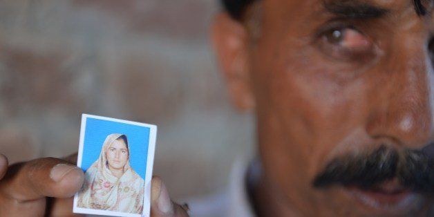 Pakistani resident Mohammad Iqbal poses for a photograph as he holds up an image of his wife Farzana Parveen, who was beaten to death with bricks by her father and other family members for marrying a man of her own choice, in Chak 367 some 40 kms from Faisalabad on May 30, 2014. Pakistani police investigating the murder of a woman bludgeoned to death outside a court have arrested four men, a senior officer said, as her husband said he wanted her killers to 'die in pain'. Farzana Parveen was killed on May 27 outside the High Court in the eastern city of Lahore by more than two dozen attackers armed with bricks, including numerous relatives, for marrying against her family's wishes. AFP PHOTO/Aamir QURESHI (Photo credit should read AAMIR QURESHI/AFP/Getty Images)